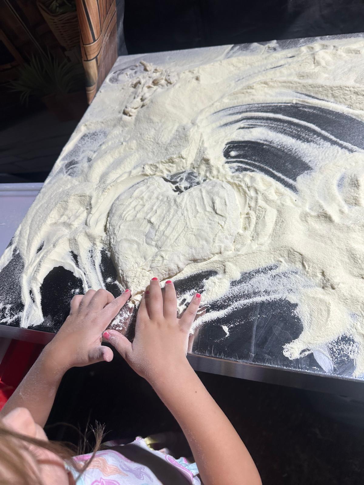 Kinderhände formen auf einer bemehlten Arbeitsfläche ein Herz aus Pizzateig
