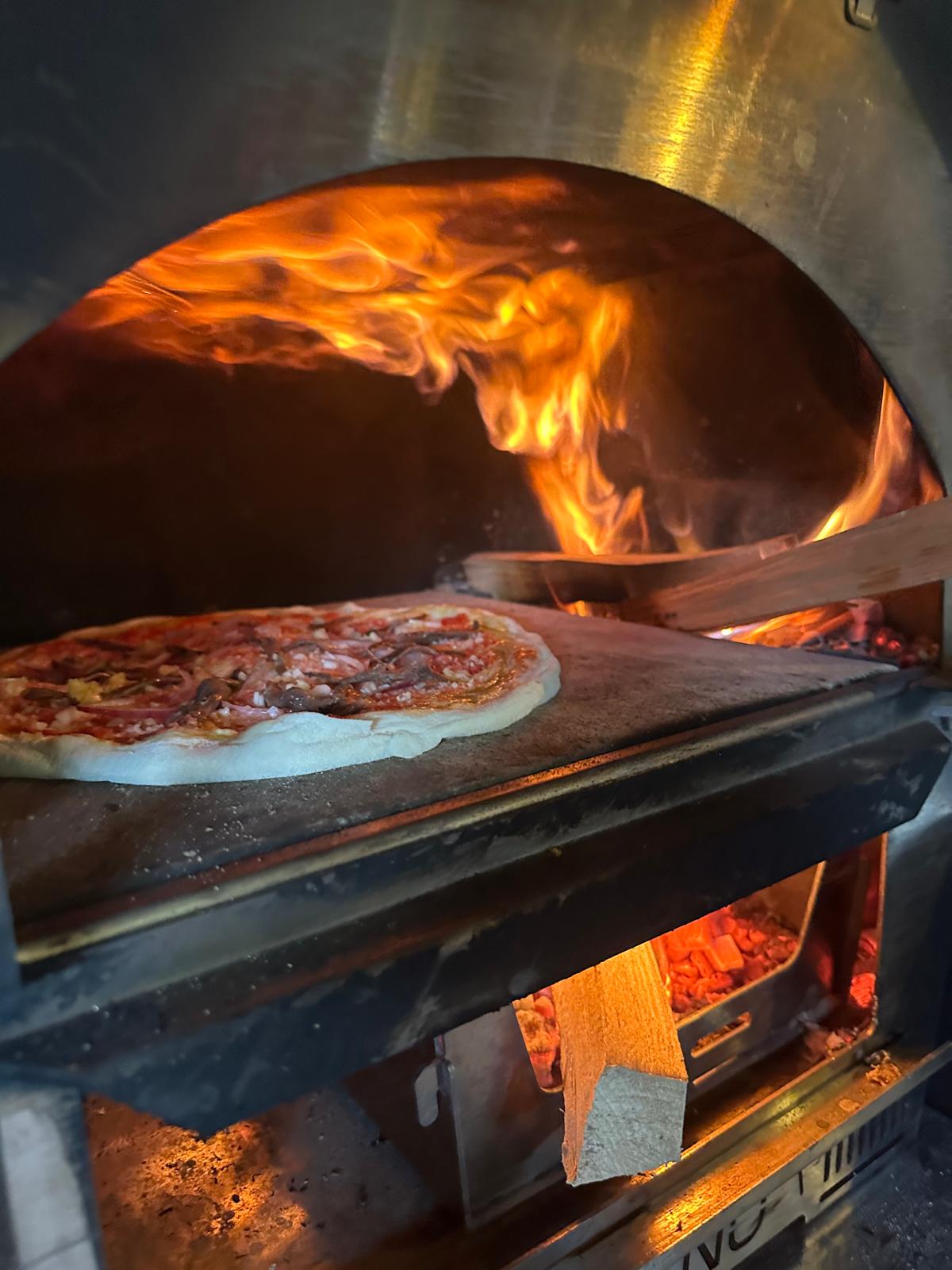 Blick in den Holzofen: Flammen schlagen über eine Pizza auf dem heißen Stein