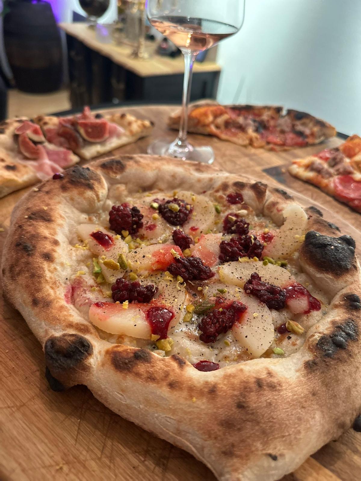 Frisch gebackene Pizzen auf einem Holztisch, dahinter ein Glas Wein