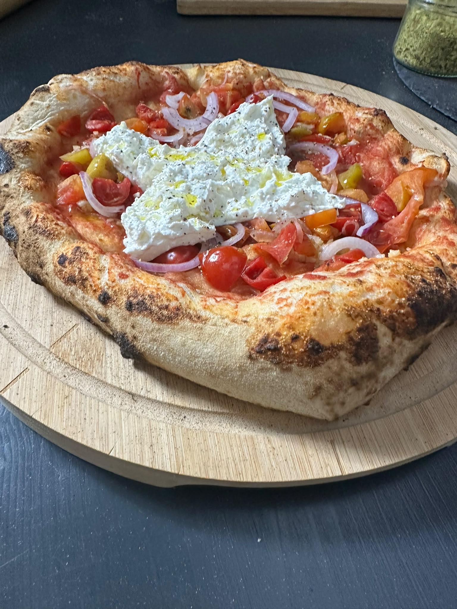 Pizza mit Burrata, Tomaten und roten Zwiebeln auf einem Holzbrett