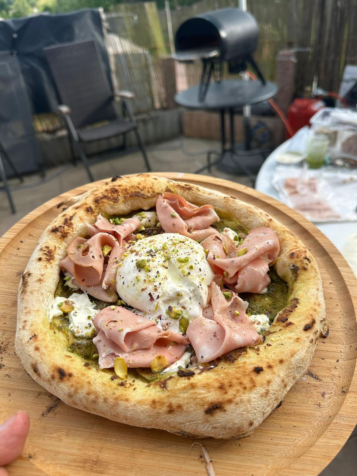 Pizza mit Mortadella, Burrata und Pistazien auf einem Holzbrett