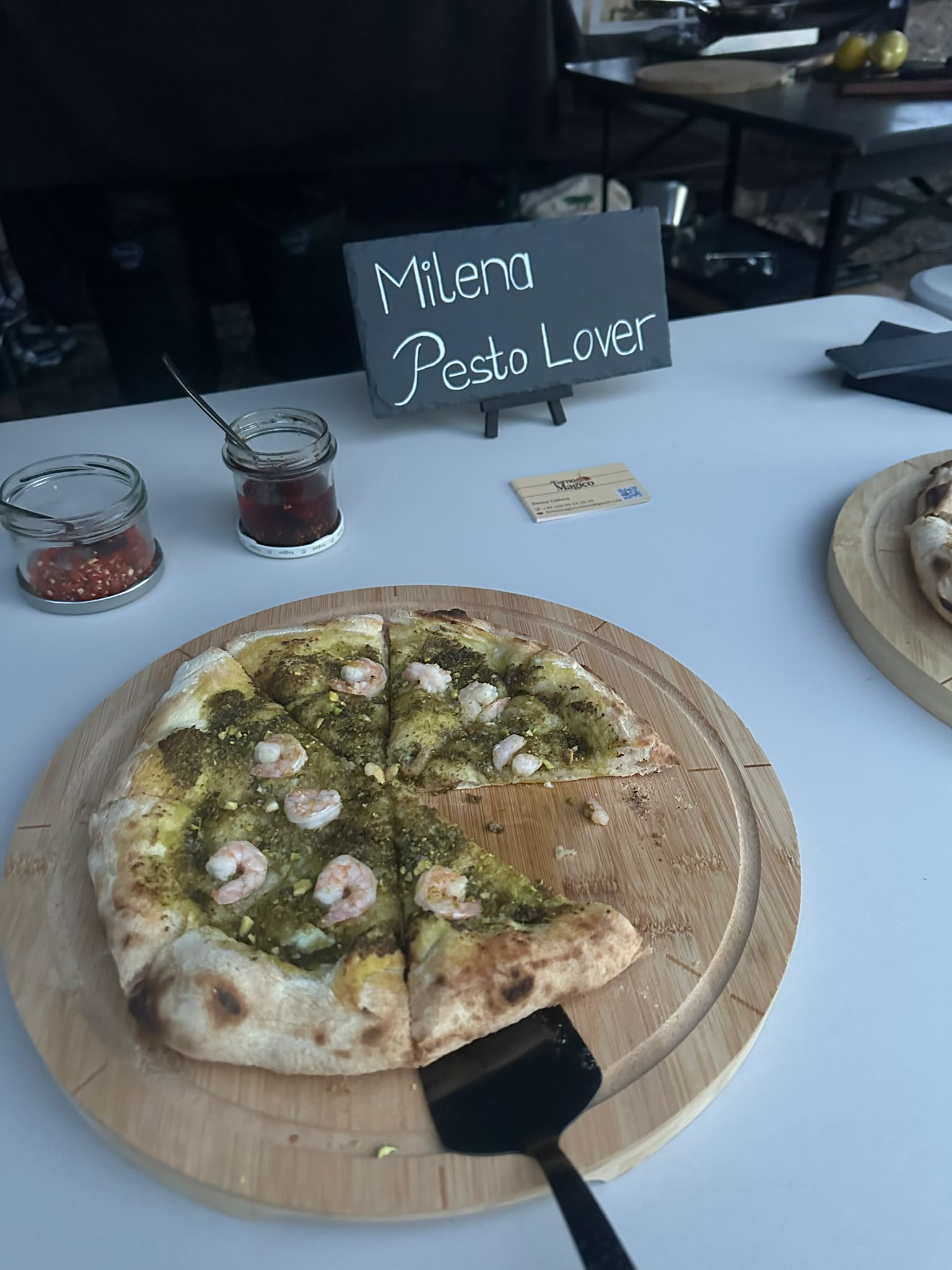 Pizza mit Pesto und Garnelen, frisch aufgeschnitten auf einem Holzbrett